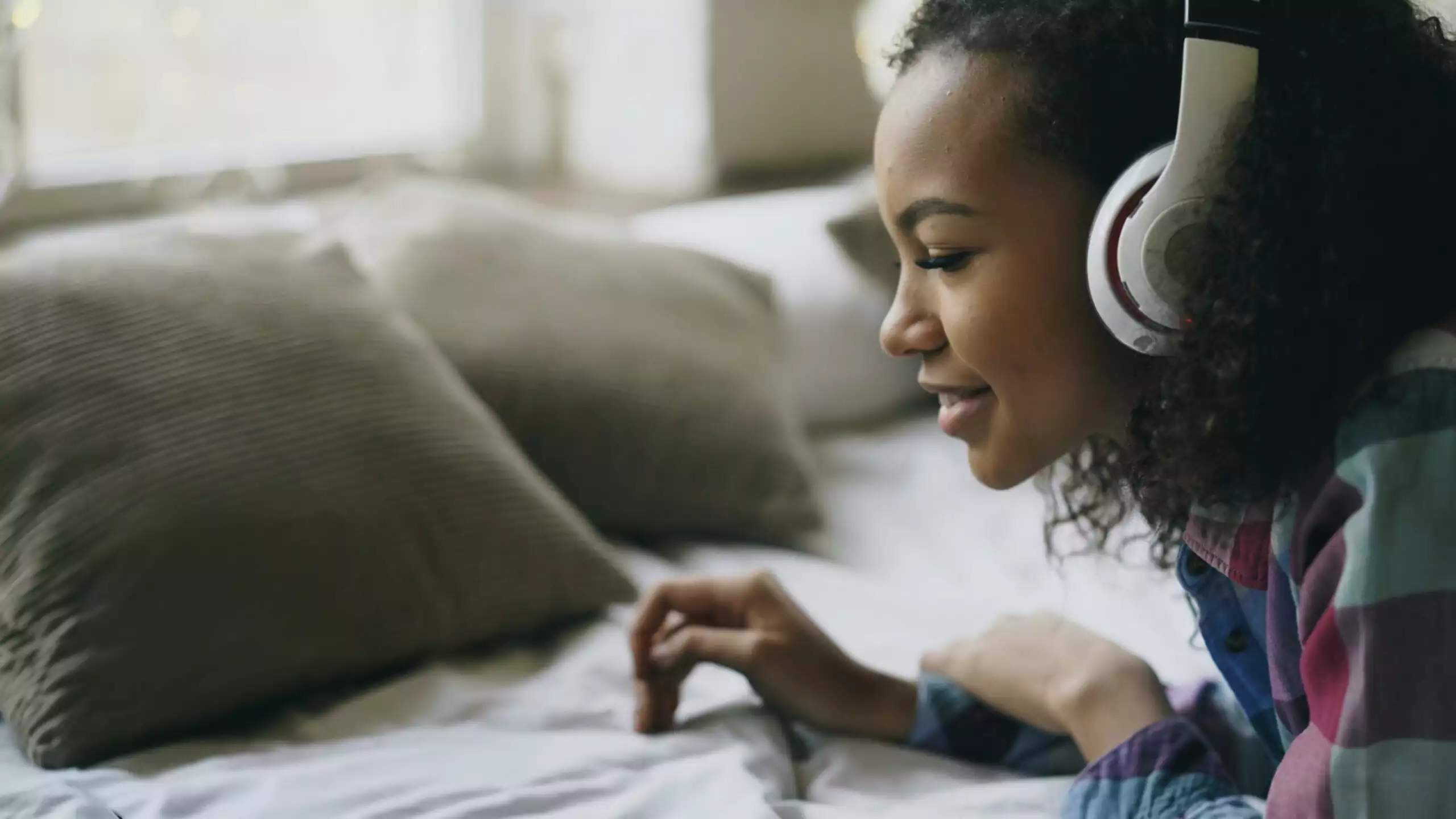Jeune femme allongée sur son lit, en train de regarder son ordinateur avec un casque
